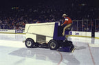 Person operating a Zamboni on an ice rink with spectators in the background, card-hover